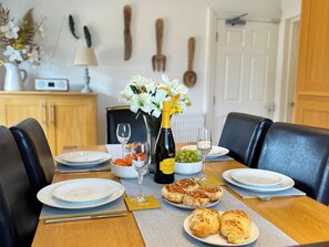 A dining table set with plates, a bottle of champagne, a vase with flowers, and pastries. - 2 bedroom accommodation in Whitby (Whitby)