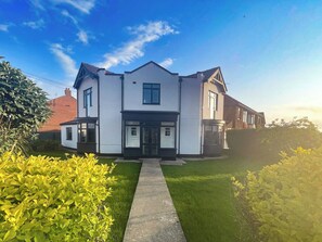 Une maison à deux étages avec une entrée centrale, une allée et une pelouse bien entretenue.