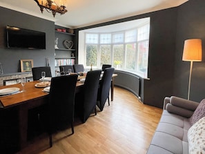 A dining area with a wooden table, black chairs, and a television mounted on the wall. - 5 bedroom accommodation in Whitby (Whitby)