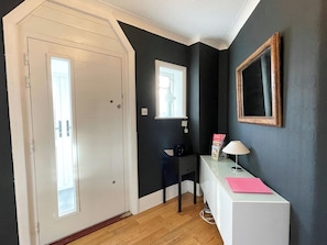 En hall med en vit dörr, ett litet bord med en lampa och en inramad spegel på väggen.