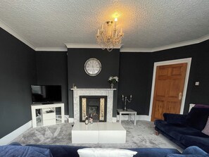 A living room with a fireplace, a television, and a chandelier. - 5 bedroom accommodation in Whitby (Whitby)