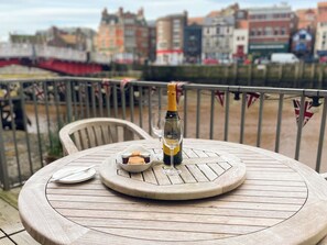 A round wooden table with a bottle of champagne, a glass, and a bowl of biscuits on a balcony overlooking a cityscape. - 1 bedroom accommodation in Whitby (Whitby)