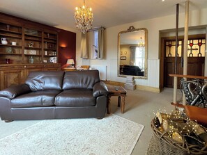 A living room with a leather sofa, a wooden coffee table, a chandelier, a large mirror, and a cat tree. - 1 bedroom accommodation in Whitby (Whitby)
