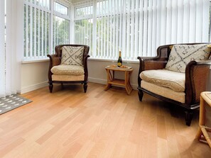 A room with two wicker armchairs, a small side table with a bottle and glasses, and a view through large windows. - 3 bedroom accommodation in Whitby (Whitby)