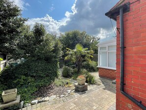 A garden with a brick wall, a palm tree, and a window. - 3 bedroom accommodation in Whitby (Whitby)