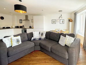 A modern living room with a grey sectional sofa, a kitchen in the background, and a dining area with yellow chairs. - 2 bedroom accommodation in Whitby (Whitby)