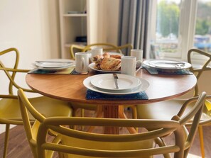 A round wooden dining table with plates, a mug, and a pastry. Yellow chairs surround the table. - 2 bedroom accommodation in Whitby (Whitby)