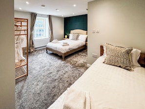 Ein Schlafzimmer mit einem Bett, einem Nachttisch, einem Fenster mit Vorhängen, einer Heizung und einem Holzregal mit Handtüchern.