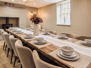 Un comedor con una mesa de madera grande dispuesta para una comida, rodeado de sillas con cojines.
