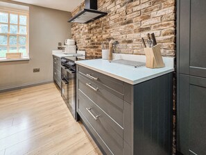 A kitchen with a brick wall, a window, and modern cabinetry. - The Farmhouse - UKC9936 (Gateshead)