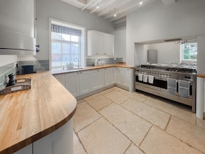 A modern kitchen with white cabinets, a wooden countertop, a stainless steel stove, and a window with a striped valance. - 5 bedroom accommodation in Walesby (Walesby)
