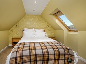 A bedroom with a sloped ceiling, a skylight, a bed with white bedding, and a plaid blanket. - The Gardener's Cottage - UKC6966 (Carnoustie)