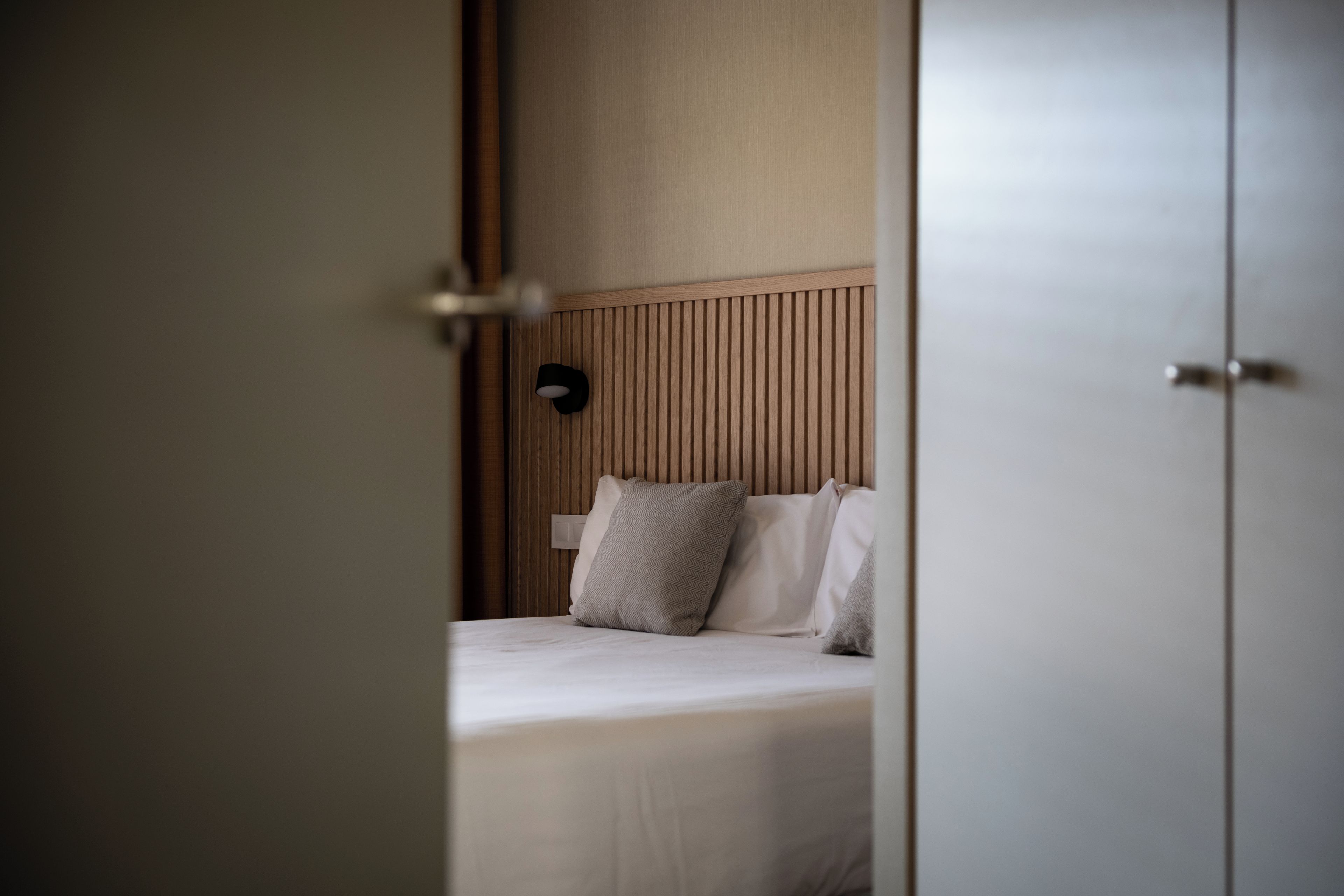 Een hotelkamer met een bed, een hoofdbord met verticale lijnen en een deur.