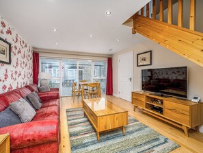 A living room with a red sofa, wooden coffee table, TV, and a staircase. - The Carriage House - UKC6967 (Carnoustie)