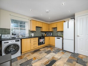 A modern kitchen with wooden cabinets, a washing machine, a microwave, and a dishwasher. - The Carriage House - UKC6967 (Carnoustie)
