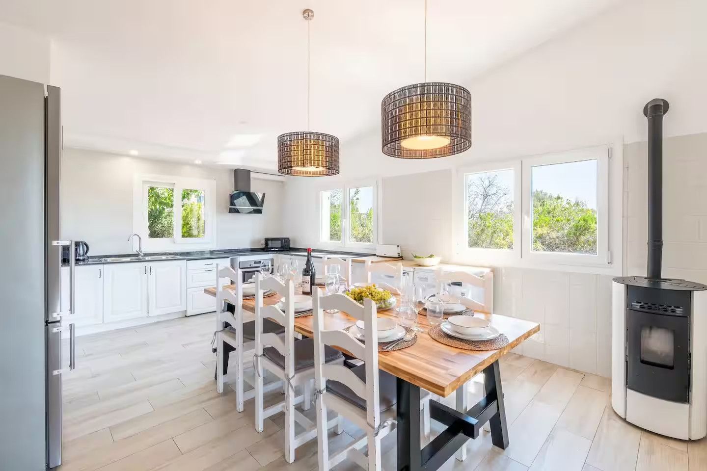 A modern kitchen with white cabinets, a wooden dining table, and a black stove.