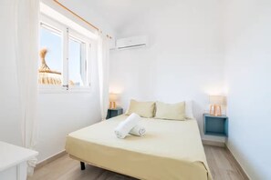 A hotel room with a bed, bedside lamps, a window with curtains, and an air conditioning unit. - VILLA CAN SUCRER  Ref: VP99 (Port de Pollença)