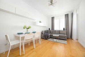 A modern living room with a dining area, a grey sofa, and a small round table. - Warsaw | Zwycięzców 40 | Comfortable Apartment | Remote Work (Warszawa)