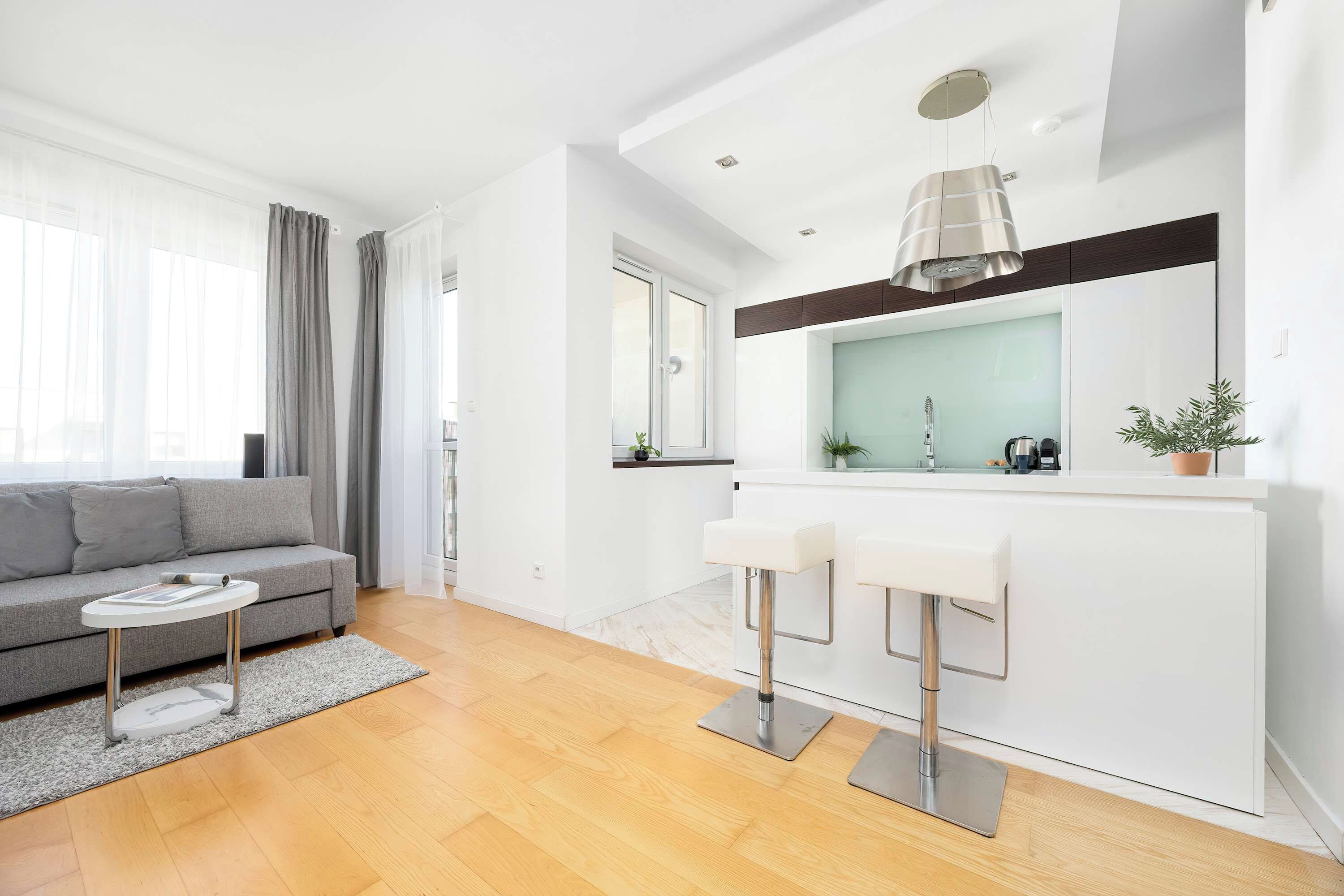 Un salon moderne avec un canapé gris, une petite table d’appoint blanche et un tapis gris.