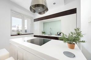 A modern kitchen with a central island, a built-in stove, a sink, and a window with a view of buildings. - Warsaw | Zwycięzców 40 | Comfortable Apartment | Remote Work (Warszawa)