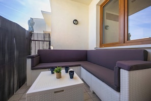 A corner seating area with a cushioned sofa, a white woven coffee table, and a potted plant. - Warsaw | Zwycięzców 40 | Comfortable Apartment | Remote Work (Warszawa)
