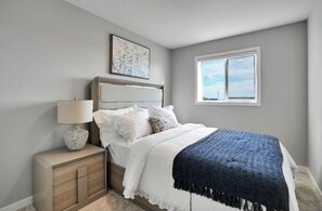 Ein Schlafzimmer mit Bett, Nachttisch, Lampe und einem Fenster mit Blick.