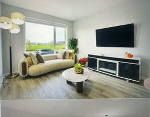 A modern living room with a sofa, a coffee table, a TV, and a plant. - Spacious and comfort| Near Airport| Easy Access to Stoney Trail & the Rockies. (calgary)