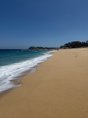 A wide sandy beach with gentle waves, a clear sky, and a building complex in the background. - Hacienda del Mar beautiful beachfront luxury resort in Cabo San Lucas, Mexico (Cabo San Lucas)