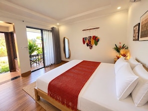 A hotel room with a large bed, a red throw blanket, white pillows, a mirror, and a view of the outdoors. - MANGO VILLAS (phu quoc)