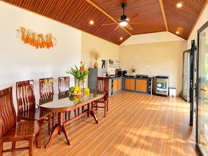 A modern kitchen with a wooden ceiling, a dining area with a glass table, and a view of the outdoors. - MANGO VILLAS (phu quoc)