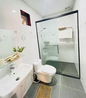 A modern bathroom with a glass-enclosed shower, a white toilet, and a sink with a glass shelf holding toiletries. - MANGO VILLAS (phu quoc)