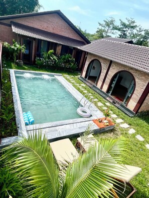 A swimming pool with a tiled deck, surrounded by a grassy area and palm trees. - MANGO VILLAS (phu quoc)