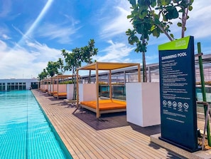 Una piscina con cubierta de madera, tumbonas y un cartel con las normas de la piscina.