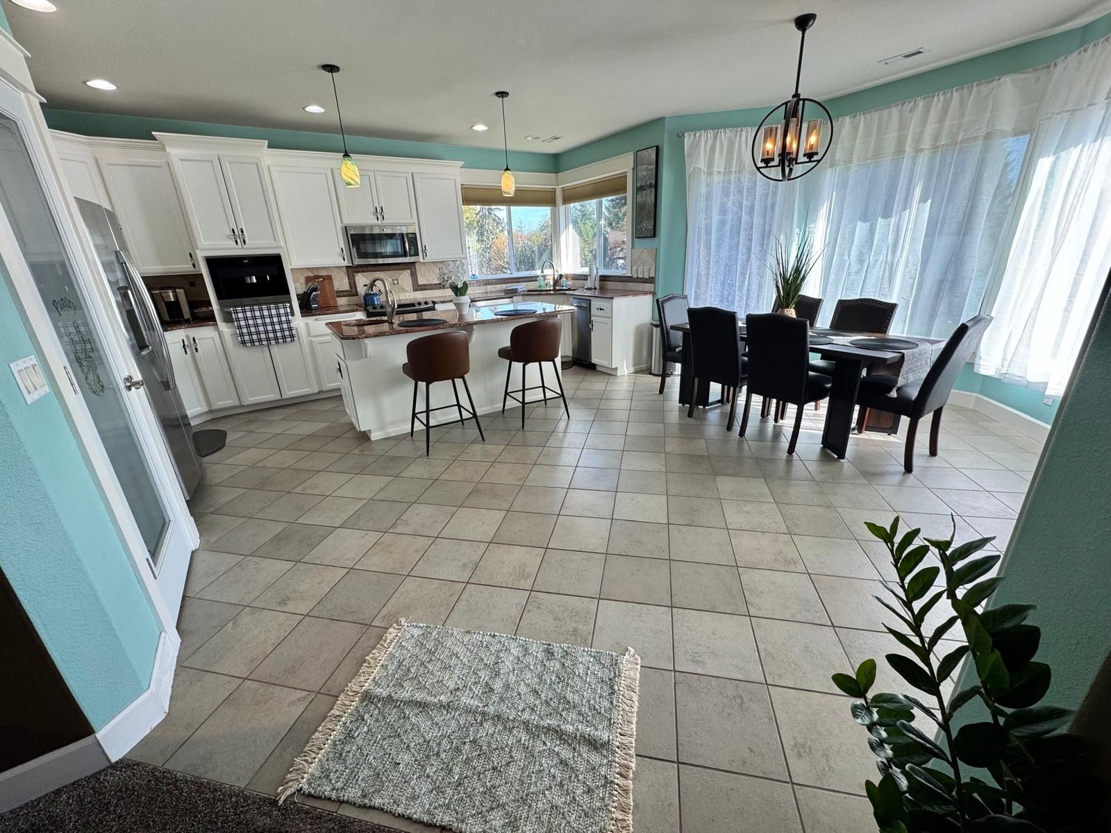 A spacious kitchen with white cabinets, a dining area with a table and chairs, and a large window with curtains.
