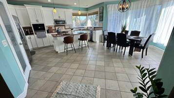 A spacious kitchen with white cabinets, a dining area with a table and chairs, and a large window with curtains.