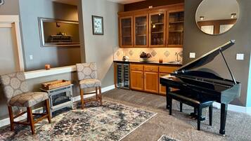 A living room with a grand piano, two armchairs, a fireplace, and a kitchen area with wooden cabinets.