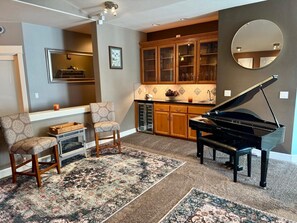 A living room with a grand piano, two armchairs, a fireplace, and a kitchen area with wooden cabinets. - Welcome to spacious, beautiful home (Graham)