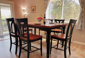 A dining area with a wooden table and chairs, a vase with flowers, and a painting on the wall. - Mali View Home in Salt Spring 
A block from ocean (Salt Spring Island)