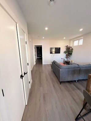 A modern interior with a hallway leading to a living area, a grey sofa, and a mounted flat-screen TV. - Nolan Hill Garden Retreat walkout basement (Calgary)