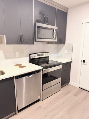 A modern kitchen with stainless steel appliances, grey cabinetry, and a white countertop. - Nolan Hill Garden Retreat walkout basement (Calgary)