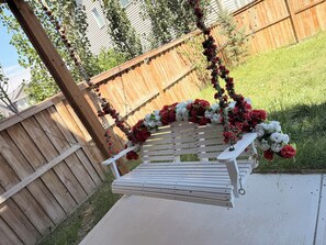 A wooden bench with a white cushion, surrounded by red and white flowers, against a wooden fence and a grassy yard. - Nolan Hill Garden Retreat walkout basement (Calgary)