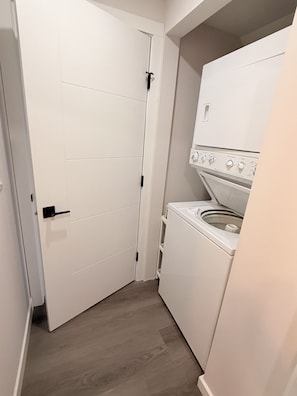 Une buanderie avec un lave-linge et un sèche-linge blancs, une porte blanche et un plancher en bois.