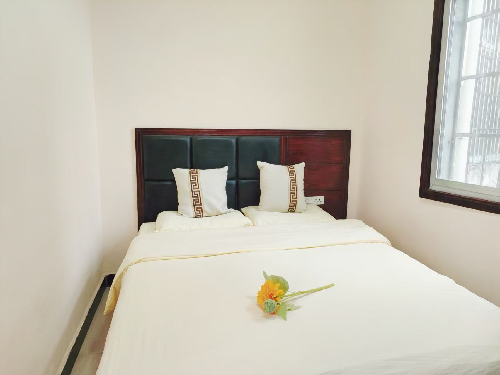 A hotel room with a bed, a headboard, and a window.