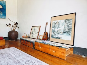 Une pièce comprenant une commode en bois, une guitare, un tableau encadré, un vase avec des branches et un tapis à motifs.