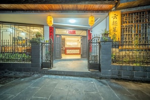 Une entrée traditionnelle avec un portail en bois, un chemin pavé et un mur décoratif orné de caractères chinois.