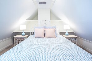 A bedroom with a bed centered under a sloped ceiling, flanked by two bedside tables with lamps, a decorative wall, and a patterned bedspread. - Furnished, Dog-Friendly Old Village Retreat w/ Fabulous Patio!  Extended-Stay, 30+ Day Leases Only (Mount Pleasant)