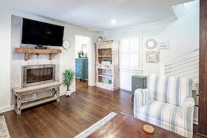 A living room with a fireplace, television, and a striped sofa. - Furnished, Dog-Friendly Old Village Retreat w/ Fabulous Patio!  Extended-Stay, 30+ Day Leases Only (Mount Pleasant)