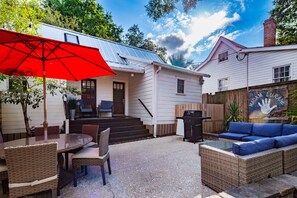 A patio area with a table and chairs, a barbecue grill, a red umbrella, and a blue sofa. - Furnished, Dog-Friendly Old Village Retreat w/ Fabulous Patio!  Extended-Stay, 30+ Day Leases Only (Mount Pleasant)
