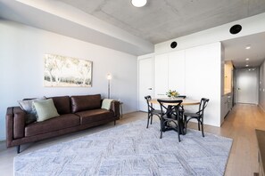 Een moderne woonruimte met een bruine leren bank, een ronde eettafel met stoelen en een groot abstract schilderij aan de muur.