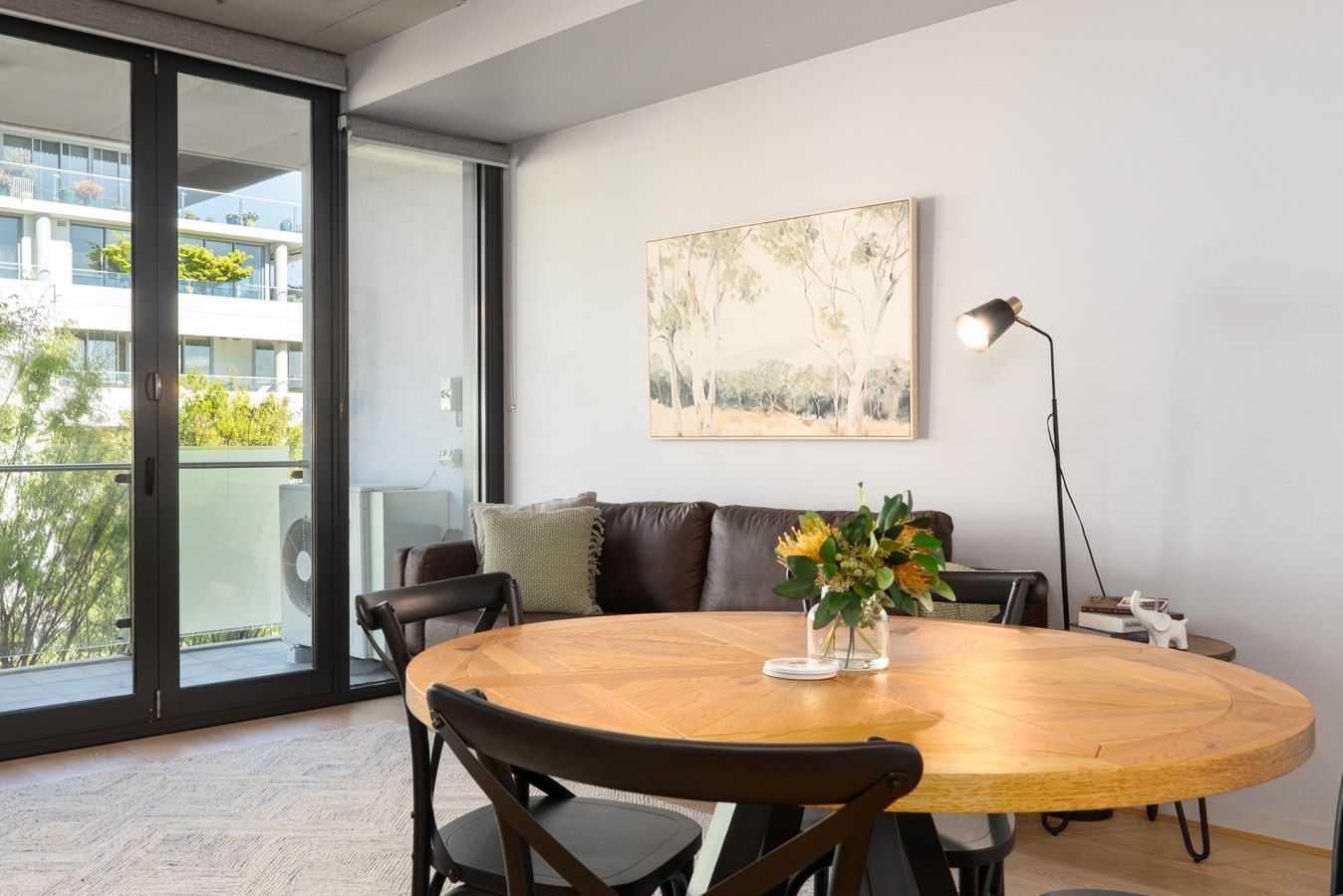 Een moderne woonkamer met een ronde houten tafel, een leren bank en een schilderij aan de muur.